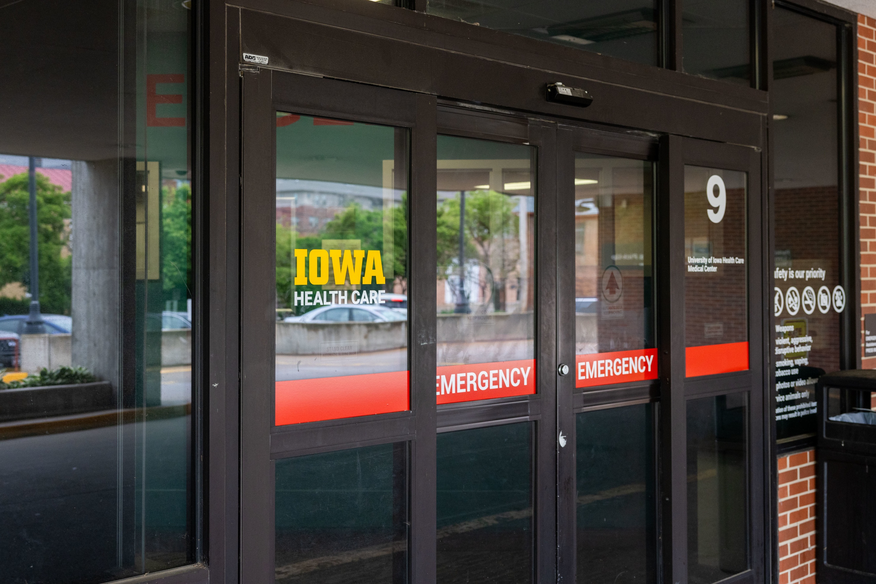 Three glass doors, one reads Iowa Health Care and all have red stripe that says Emergency in white letters. 