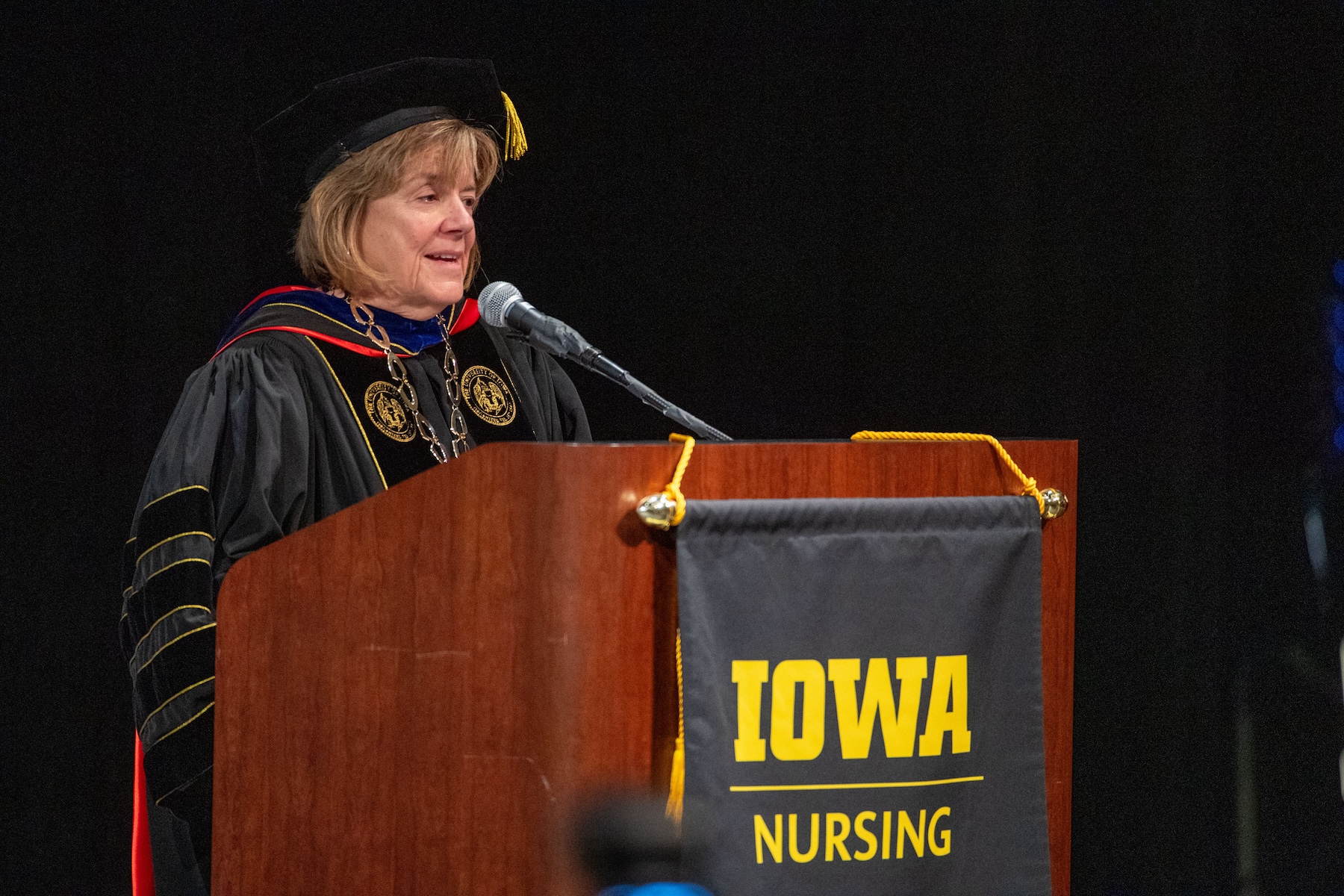 UI President Barbara Wilson stands at microphone with Iowa Nursing logo on front. 