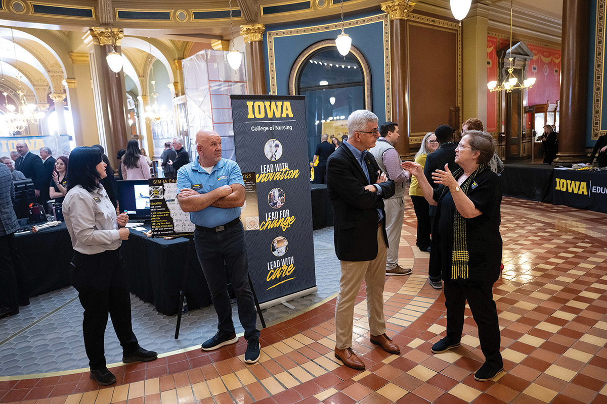Small groups of people stand around talking. Ornate floors and walls indicate they are in the state capitol building.