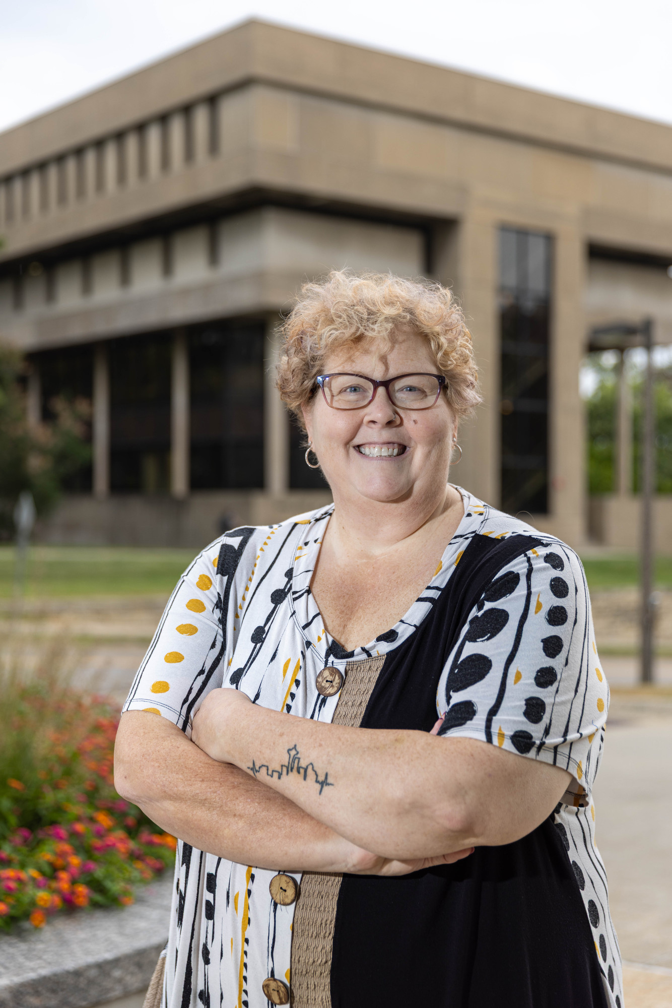 Smiling woman stands with arms crossed in front of nursing building. 