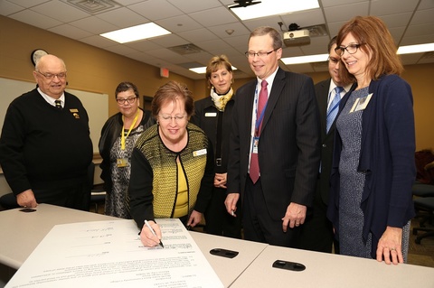 Dean Zerwic signing the RN to BSN 3+1 agreement, surrounded by others in the background