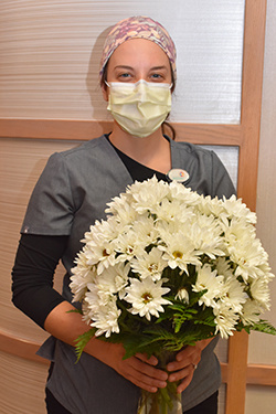 Woman in mask and scrubs holds a large bouquet of daisies. 