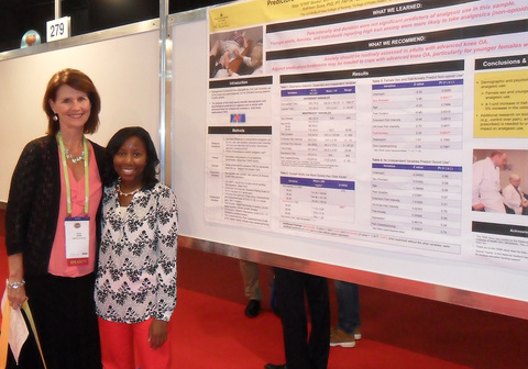 Two women stand in front of a research poster, one arm around each other, smiling. 