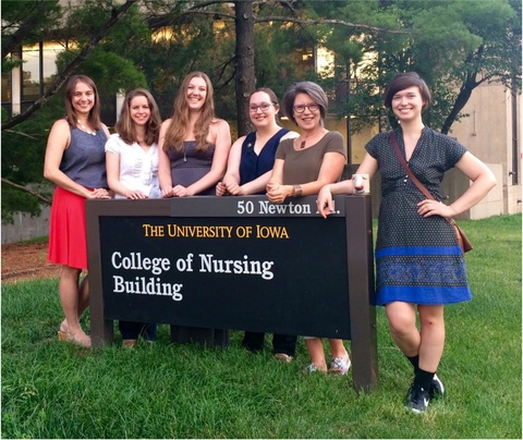 A group of smiling women stand around the College of Nursing sign. 