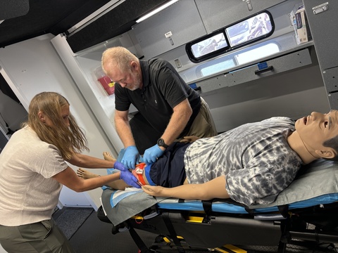 two people apply a tourniquet to a simulated patients leg