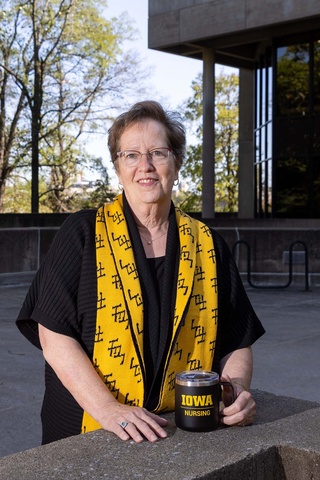 Woman in black with a black and gold scarf holding an Iowa Nursing mug.