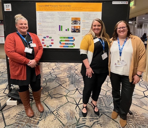 Three people stand in front of a poster in a conference setting. 