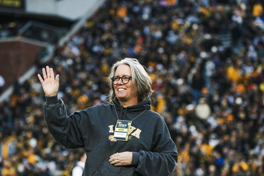 Woman in black sweatshirt waves from the football field. Fans can be seen in background. 