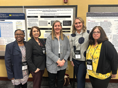 A group of five people stand together smiling at camera in front of research posters. 