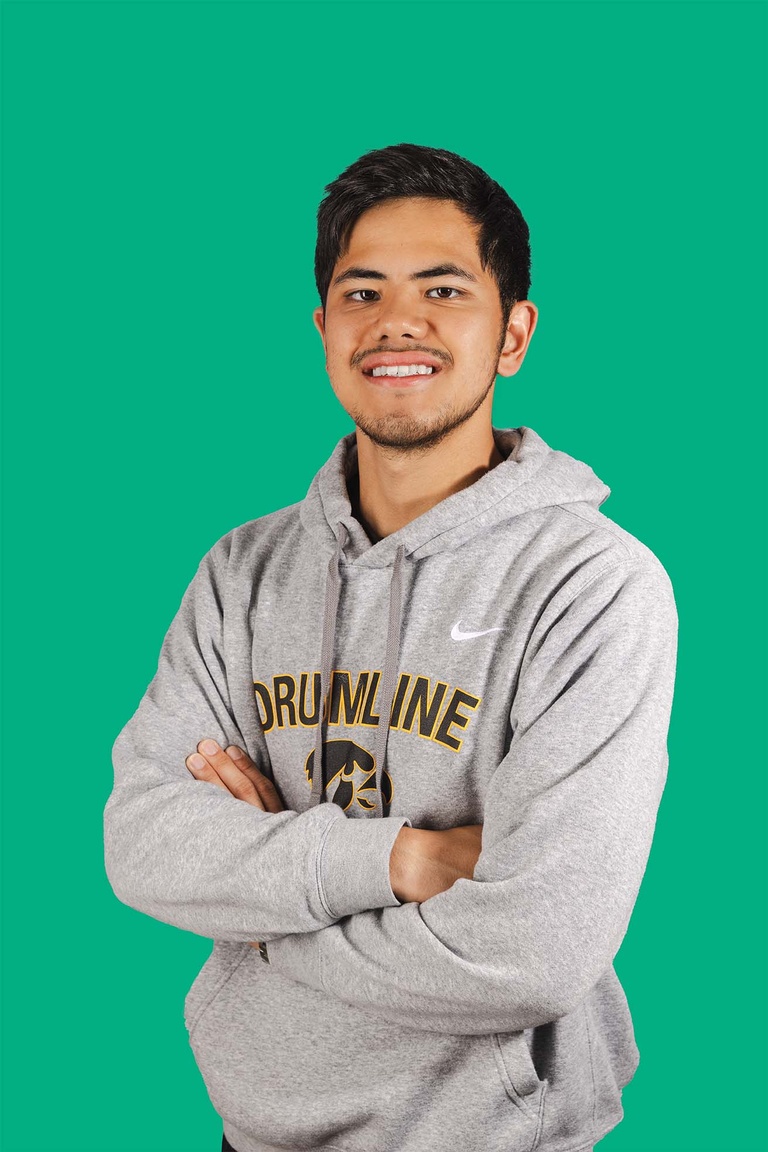 Man wearing grey sweatshirt poses with arms crossed, smiling at camera. The background behind him is green.