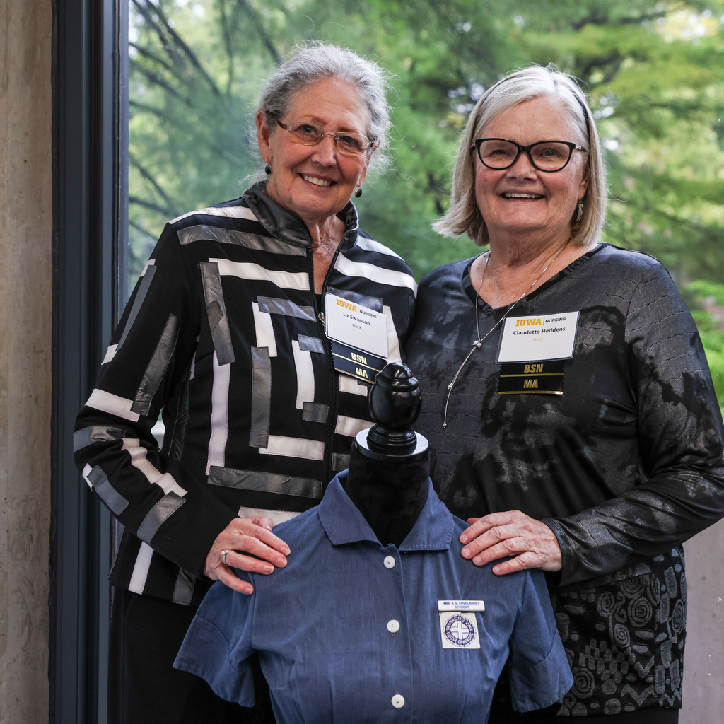 Two women stand behind an old College of Nursing uniform at the 125th anniversary of the college