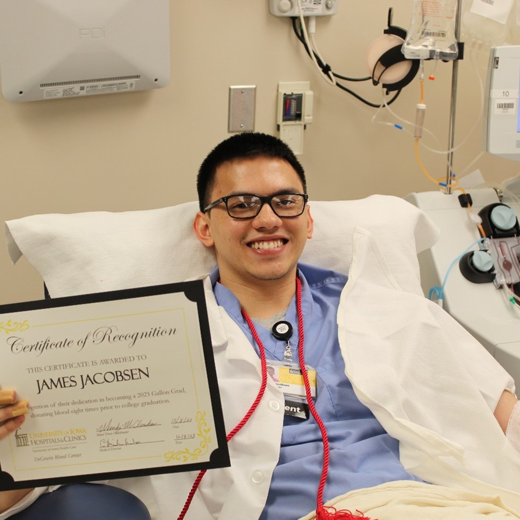 Smiling student giving blood and holding up certificate. 