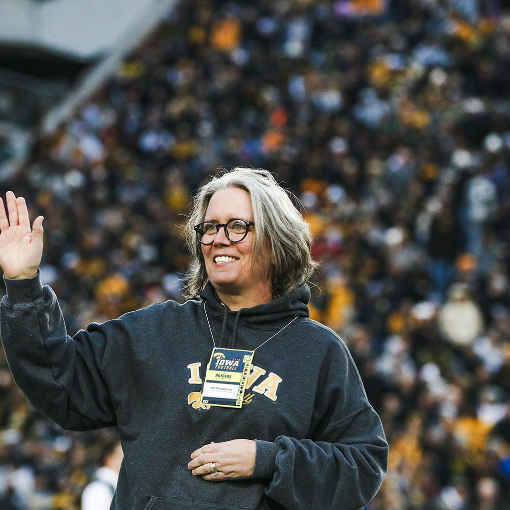 Woman in black sweatshirt waves from the football field. Fans can be seen in background.