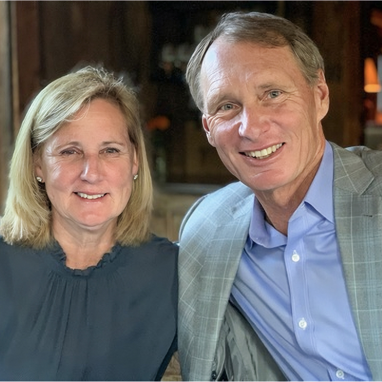 Portrait of Andy and Susie Code sitting together, fireplace in background.