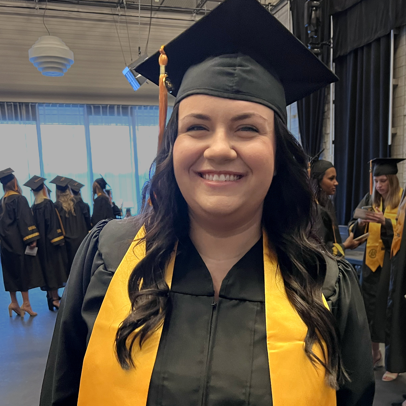 Woman in black graduation cap and gown with gold Iowa stole smiles at camera.