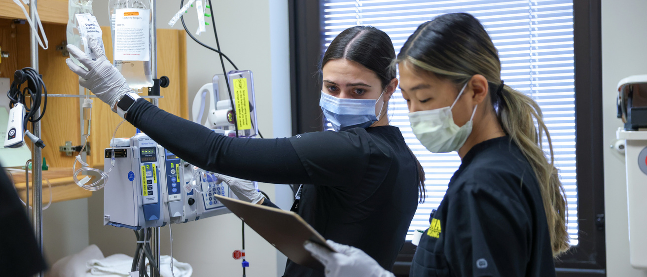 Two students nurses consult a chart and adjust an iv
