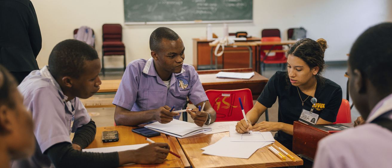 Students sit at desks in a group writing