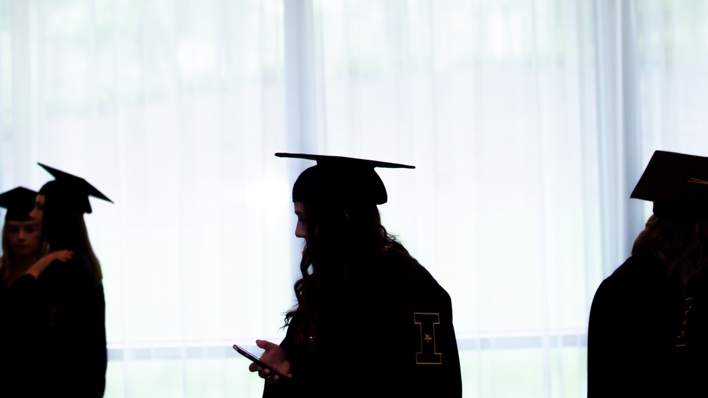 Three graduates in cap and gown are silhouetted against a window. 