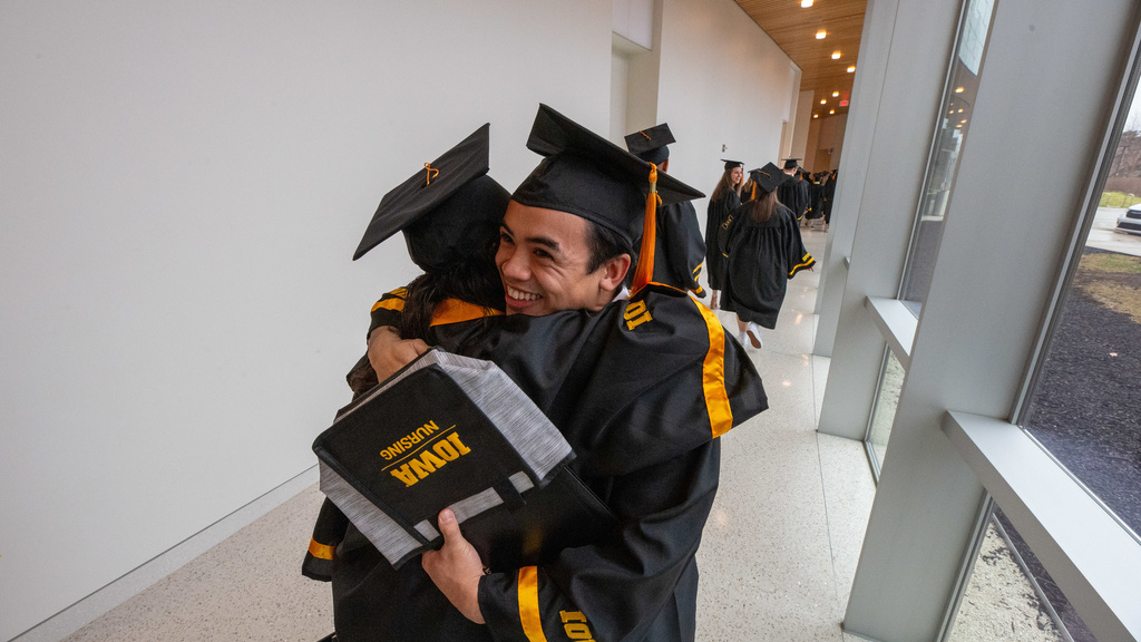 Two students in caps and gowns hug in the hallway after commencement. 