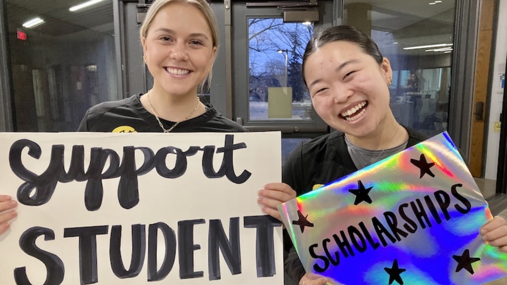 Two smiling students with signs that read support student scholarships. 