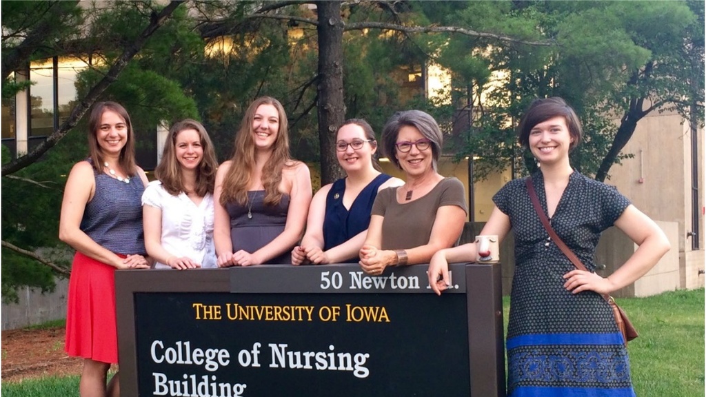 A group of smiling women stand around the College of Nursing sign. 
