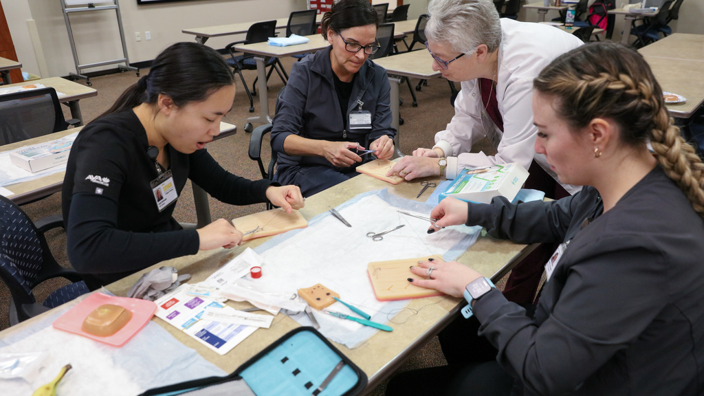 three students and a faculty work on sutures at a table