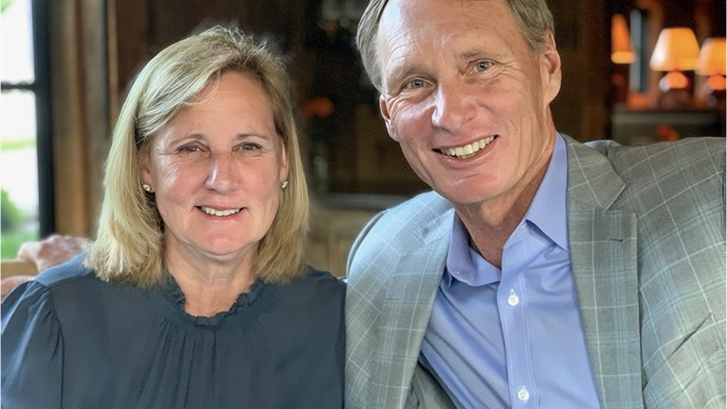 Portrait of Andy and Susie Code sitting together, fireplace in background. 