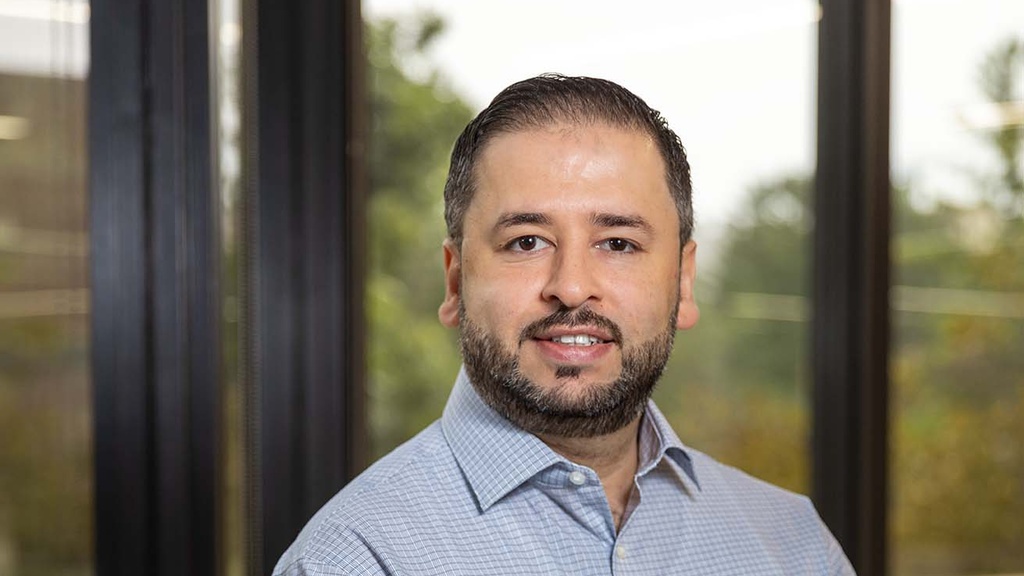 portrait of a man standing in front of large windows, hands crossed in front of him. 