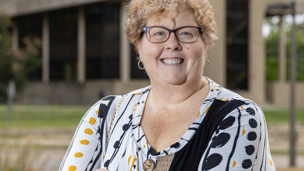 Smiling woman stands with arms crossed in front of nursing building. 