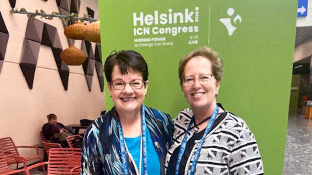 two smiling women in front of green banner