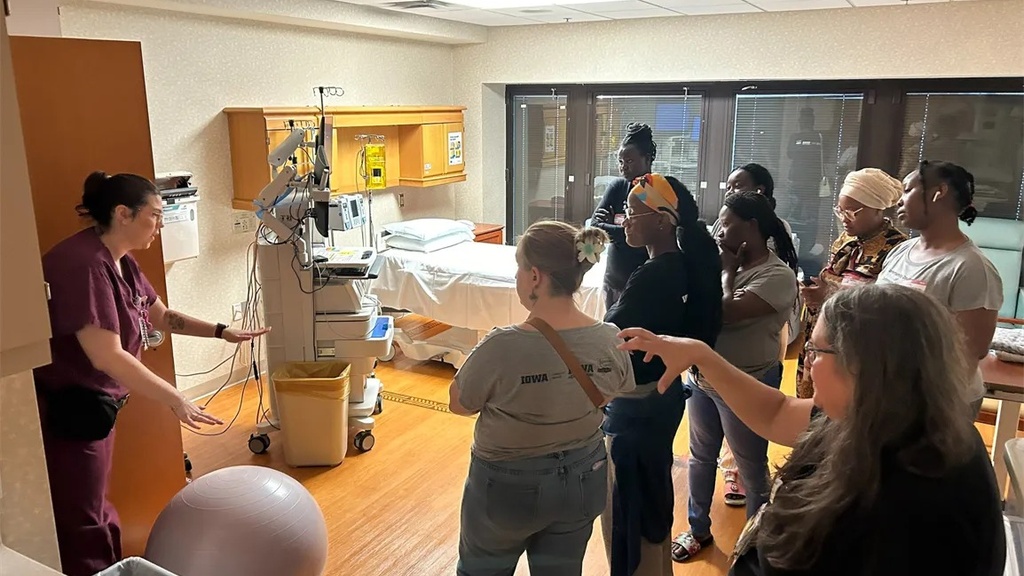 In a hospital room, a group watches a person in scrubs demonstrate a machine. 