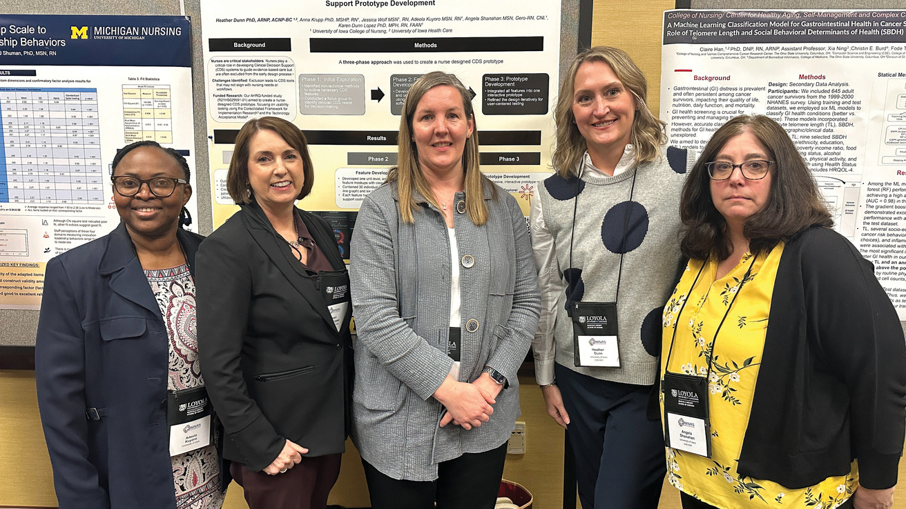 A group of five people stand together smiling at camera in front of research posters.
